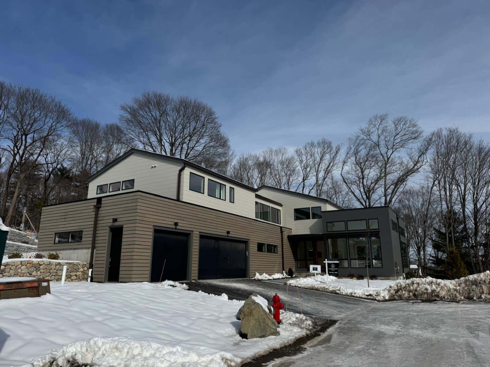 Modern two-story home with gray siding and dark garage doors after a snowfall